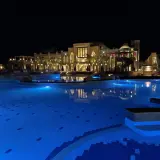 Nocny basen z niebieskim podświetleniem i luksusowym budynkiem hotelu Lazuli Marsa Alam w tle.