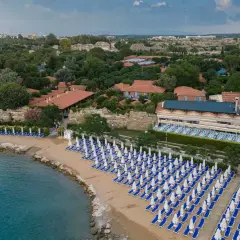 Piękna plaża z rzędami leżaków i parasoli, obok hotel z ogrodem i widokiem na morze. Idealne miejsce na wakacje.