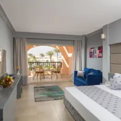 Pokój hotelowy z balkonem, jak z pałacu Ali Baby. Wygodne łóżko, sofa i stolik z widokiem na palmy.