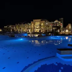 Nocny basen z niebieskim podświetleniem i luksusowym budynkiem hotelu Lazuli Marsa Alam w tle.