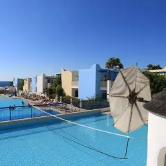 Słoneczny dzień w Eleni Holiday Village. Baseny, leżaki, kolorowe budynki i widok na morze. Idealne miejsce na wakacje.