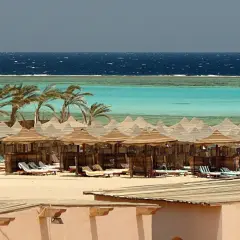 Majowa pogoda w Marsa Alam: palmy, turkusowe morze i plaża z leżakami pod słomianymi parasolami.