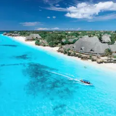 Idealny dzień na Zanzibarze: turkusowa woda, biała plaża i łódź pełna ludzi.