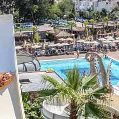 Dwie osoby zjeżdżają na pontonie ze zjeżdżalni wodnej w Atlantique Holiday Club. W tle basen i leżaki.