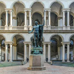Dziedziniec Pinacoteca di Brera z rzeźbą w centrum i arkadowymi galeriami.