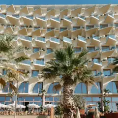 Nowoczesny hotel z białymi, geometrycznymi balkonami i palmami przed fasadą. Epidamn white sensation.