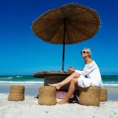 Kobieta w białej sukience siedzi pod parasolem na plaży Djerby. Uważaj na słońce i upał, pijąc orzeźwiający napój.