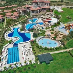 Widok z lotu ptaka na Serra Palace w Turcji: rozległy kompleks basenów, zjeżdżalni wodnych, kortów tenisowych i budynków hotelowych otoczony zielenią.