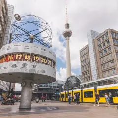 Wieża telewizyjna Berlin góruje nad placem z zegarem światowym i żółtym tramwajem.