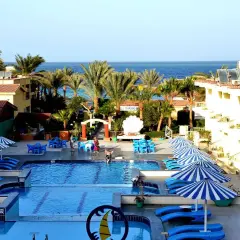 Relaks na piaszczystej plaży w Hurghadzie, basen z leżakami i parasolami, palmy i morze w tle.