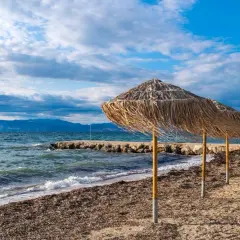 Słomiane parasole na plaży Angela Beach Korfu, morze i góry w tle.