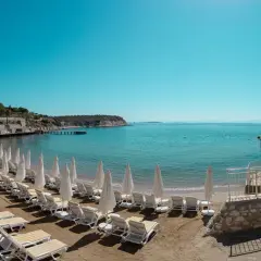 Plaża z rzędami leżaków i parasoli w Anadolu Hotels Didim Club. Błękitne morze i spokojne niebo zapraszają do relaksu.