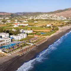 Hotel Solimar White Pearl, białe budynki z basenem i leżakami, rozciągają się wzdłuż ciemnej plaży i turkusowego morza.