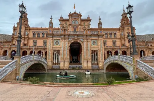 Majestatyczny plac hiszpański w Sewilli z kanałem i łódkami. Architektura zachwyca detalami.