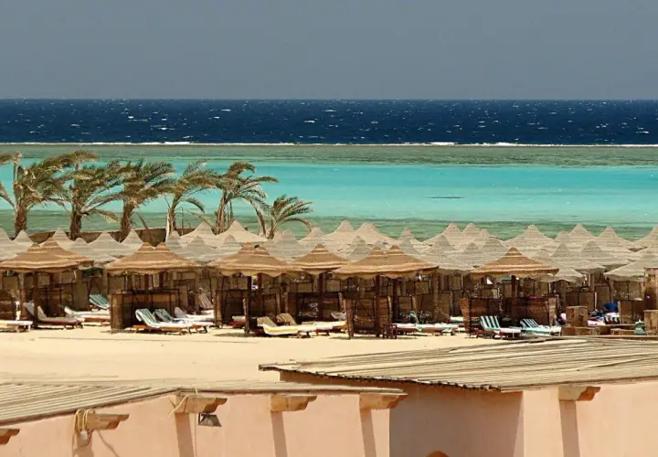 Majowa pogoda w Marsa Alam: palmy, turkusowe morze i plaża z leżakami pod słomianymi parasolami.