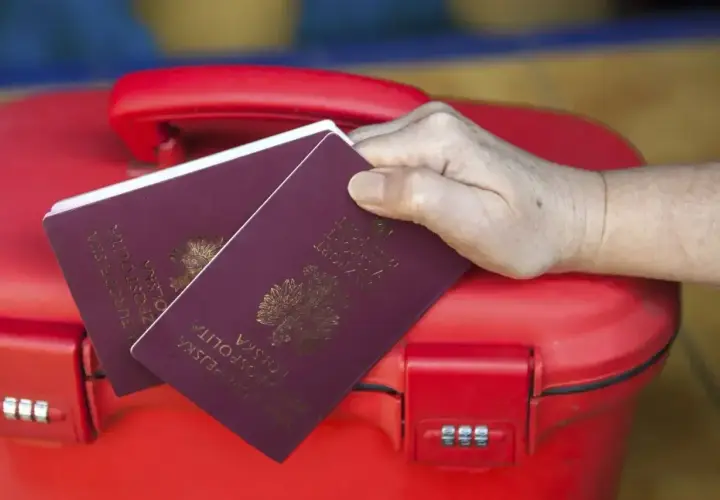 Dwa paszporty na czerwonej walizce. Zastanawiasz się, paszport dla dziecka ile ważny?