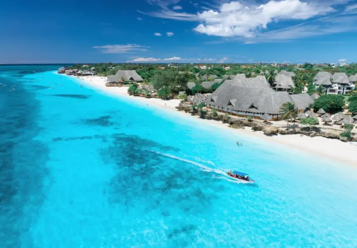Idealny dzień na Zanzibarze: turkusowa woda, biała plaża i łódź pełna ludzi.