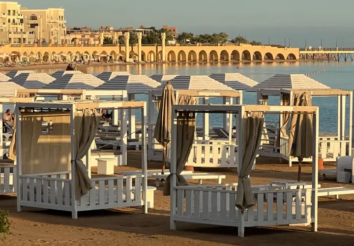 Piękna pogoda w Egipcie w styczniu. Leżaki i baldachimy na plaży, w tle budynki i morze.