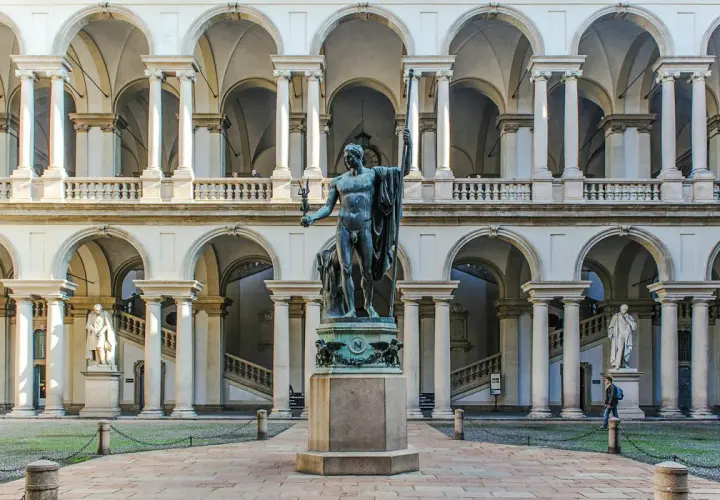 Dziedziniec Pinacoteca di Brera z rzeźbą w centrum i arkadowymi galeriami.