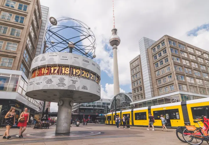 Wieża telewizyjna Berlin góruje nad placem z zegarem światowym i żółtym tramwajem.