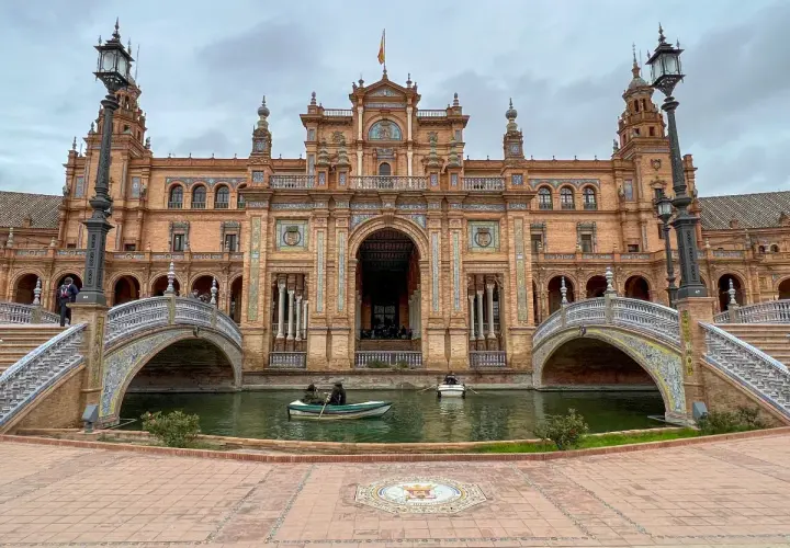 Majestatyczny plac hiszpański w Sewilli z kanałem i łódkami. Architektura zachwyca detalami.