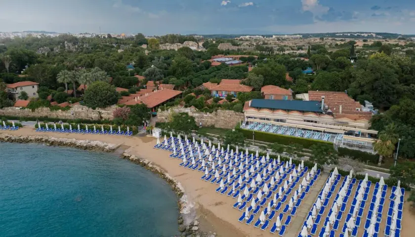 Piękna plaża z rzędami leżaków i parasoli, obok hotel z ogrodem i widokiem na morze. Idealne miejsce na wakacje.