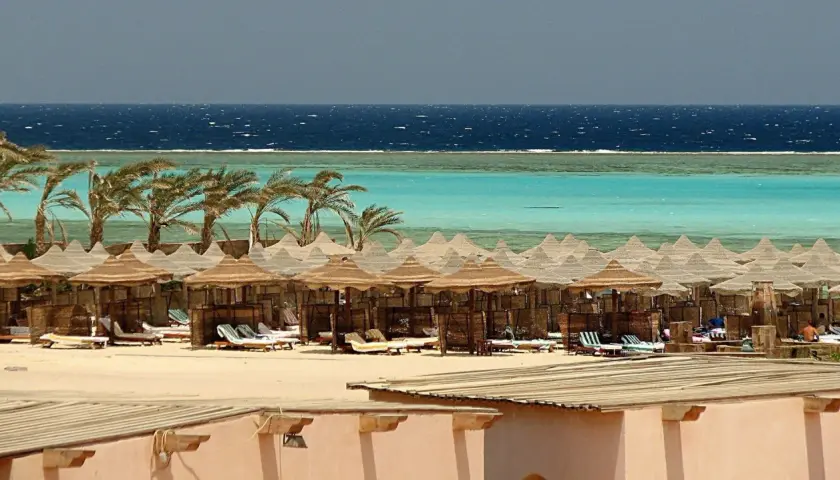 Majowa pogoda w Marsa Alam: palmy, turkusowe morze i plaża z leżakami pod słomianymi parasolami.
