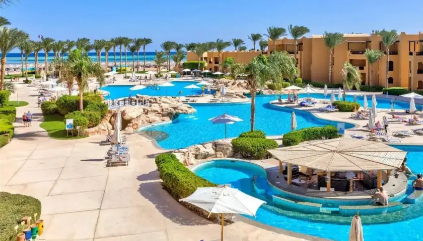 Słoneczny dzień w Stella Beach Resort & Spa Makadi Bay. Goście relaksują się przy basenach, pod palmami i parasolami.