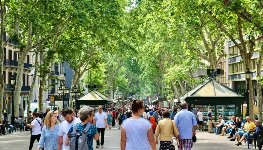 Spacerem po La Rambla w Barcelonie. Ludzie cieszą się słoneczną pogodą w marcu, spacerując wśród drzew i kiosków.