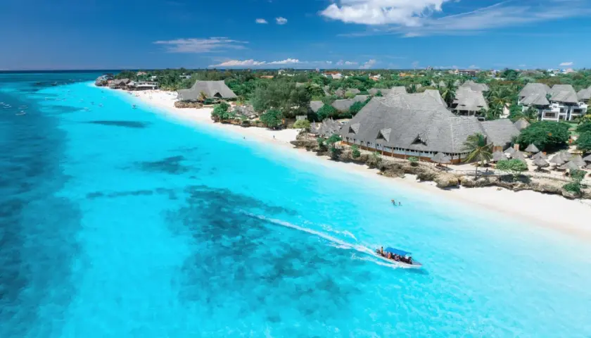 Idealny dzień na Zanzibarze: turkusowa woda, biała plaża i łódź pełna ludzi.