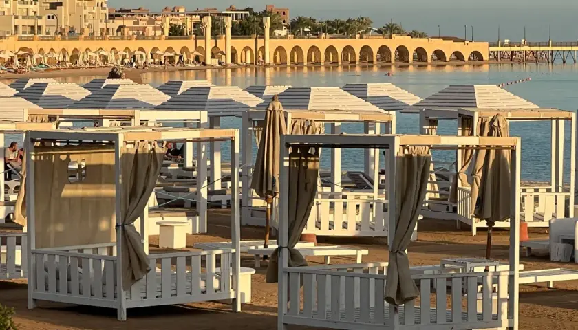 Piękna pogoda w Egipcie w styczniu. Leżaki i baldachimy na plaży, w tle budynki i morze.
