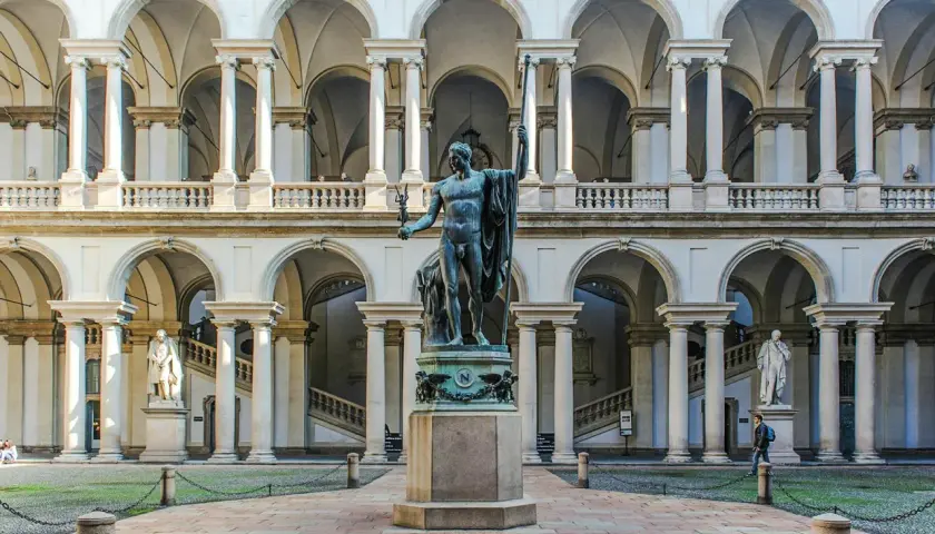 Dziedziniec Pinacoteca di Brera z rzeźbą w centrum i arkadowymi galeriami.