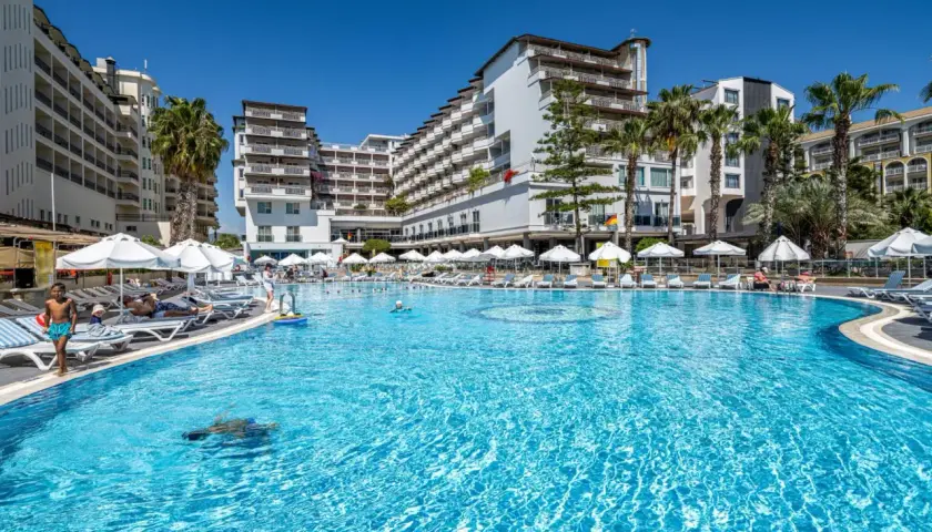 Basen hotelowy Granada Luxury Okurcalar, z leżakami, parasolami i palmami. Dzieci pluskają się w wodzie.
