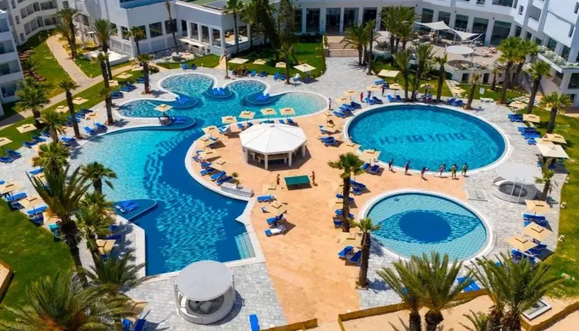 Luksusowy kompleks basenów z palmami i leżakami, z napisem "Blue Beach" w wodzie. Idealne miejsce na wakacje w Monastyrze.