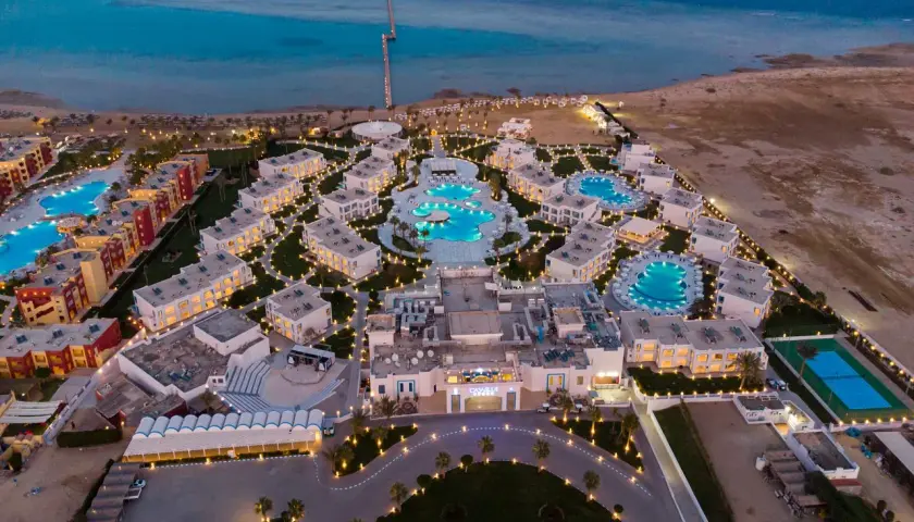Widok z lotu ptaka na luksusowy resort Casa Blue, z basenami, budynkami i morzem w tle, oświetlony wieczorem.