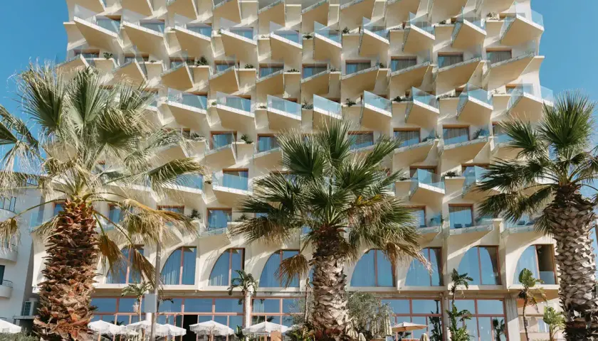 Nowoczesny hotel z białymi, geometrycznymi balkonami i palmami przed fasadą. Epidamn white sensation.
