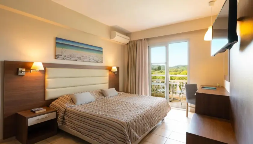 Przytulny pokój w Mitsis Messonghi Beach z widokiem na zieleń. Duże łóżko, klimatyzacja i balkon zapraszają do relaksu.