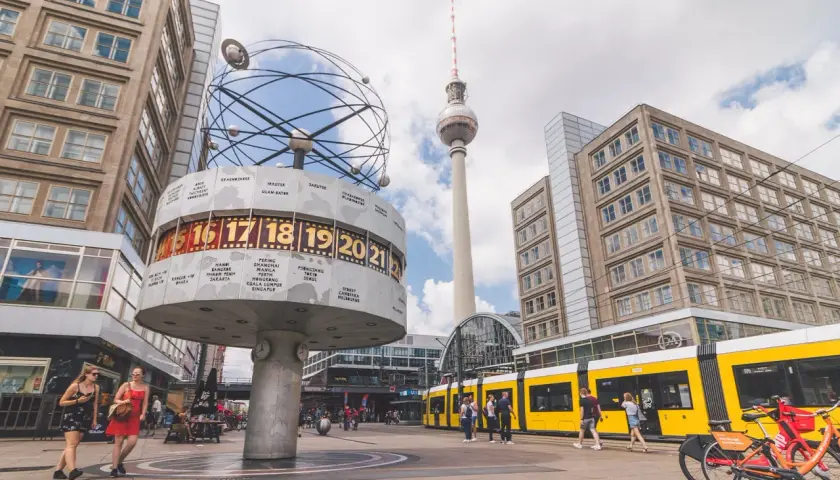 Wieża telewizyjna Berlin góruje nad placem z zegarem światowym i żółtym tramwajem.