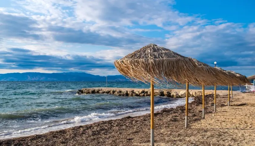 Słomiane parasole na plaży Angela Beach Korfu, morze i góry w tle.