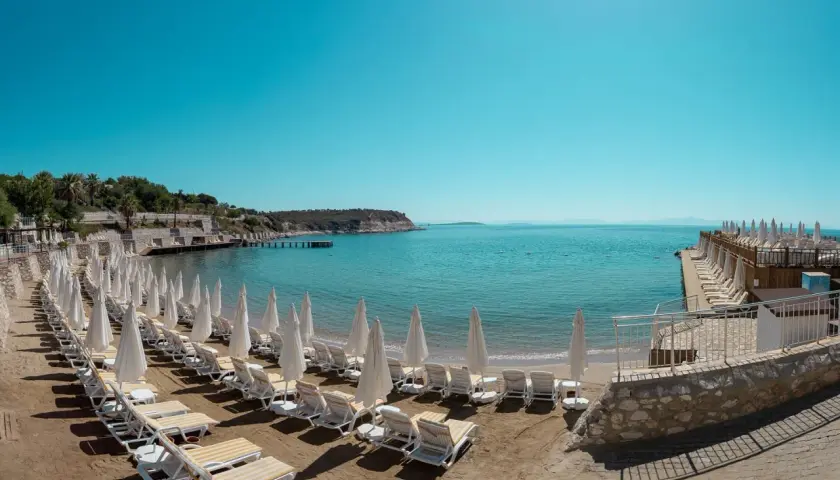 Plaża z rzędami leżaków i parasoli w Anadolu Hotels Didim Club. Błękitne morze i spokojne niebo zapraszają do relaksu.
