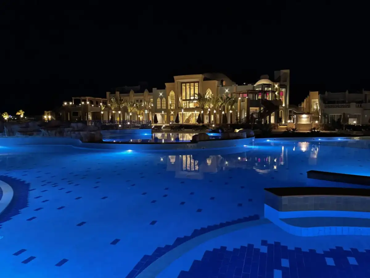 Nocny basen z niebieskim podświetleniem i luksusowym budynkiem hotelu Lazuli Marsa Alam w tle.