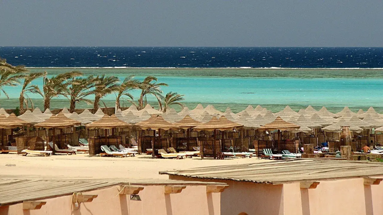Majowa pogoda w Marsa Alam: palmy, turkusowe morze i plaża z leżakami pod słomianymi parasolami.