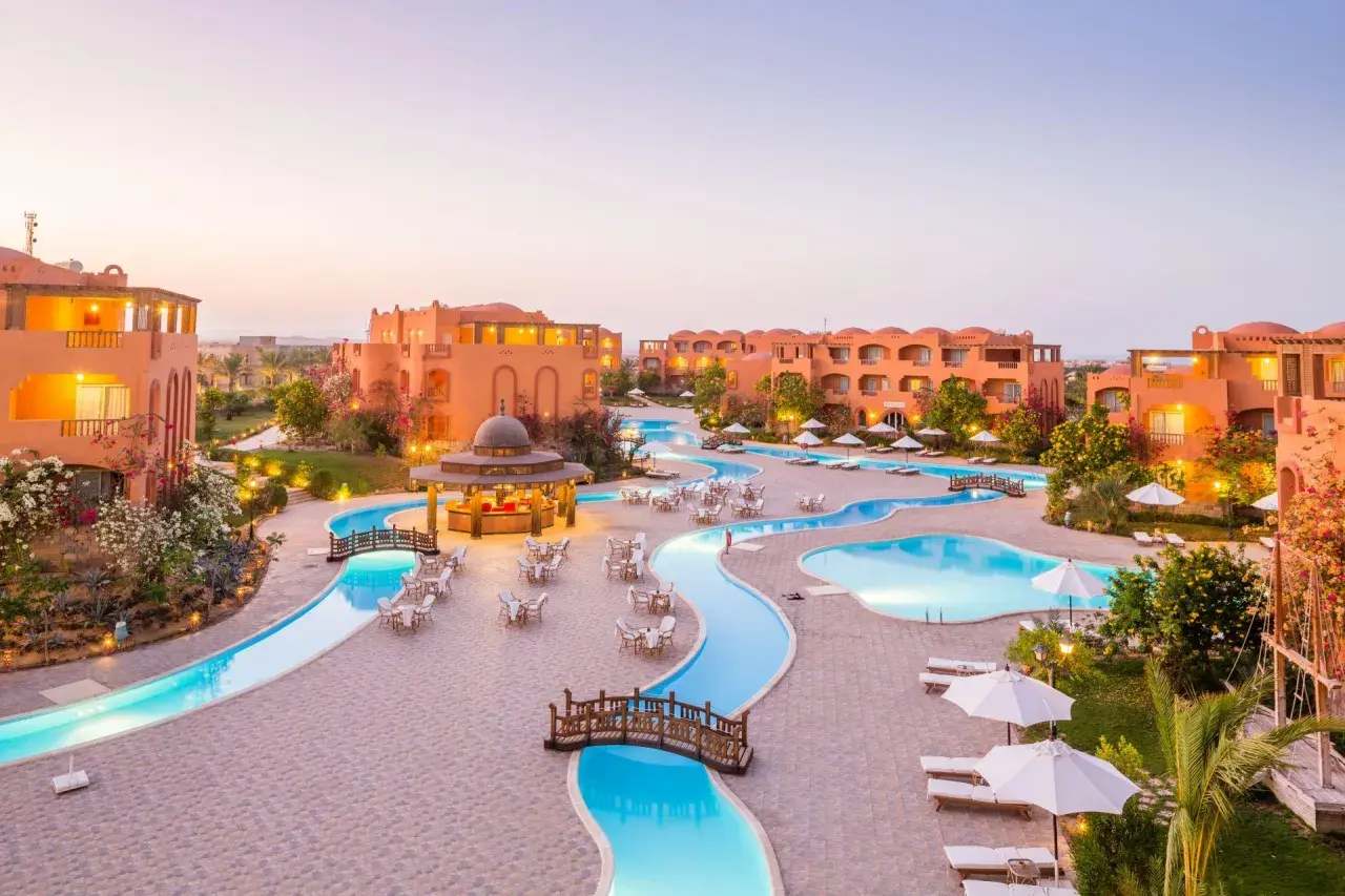 Dream Lagoon & Aqua Park Resort: malowniczy widok na kompleks basenów i budynków w ciepłych barwach, z mostkami i leżakami.