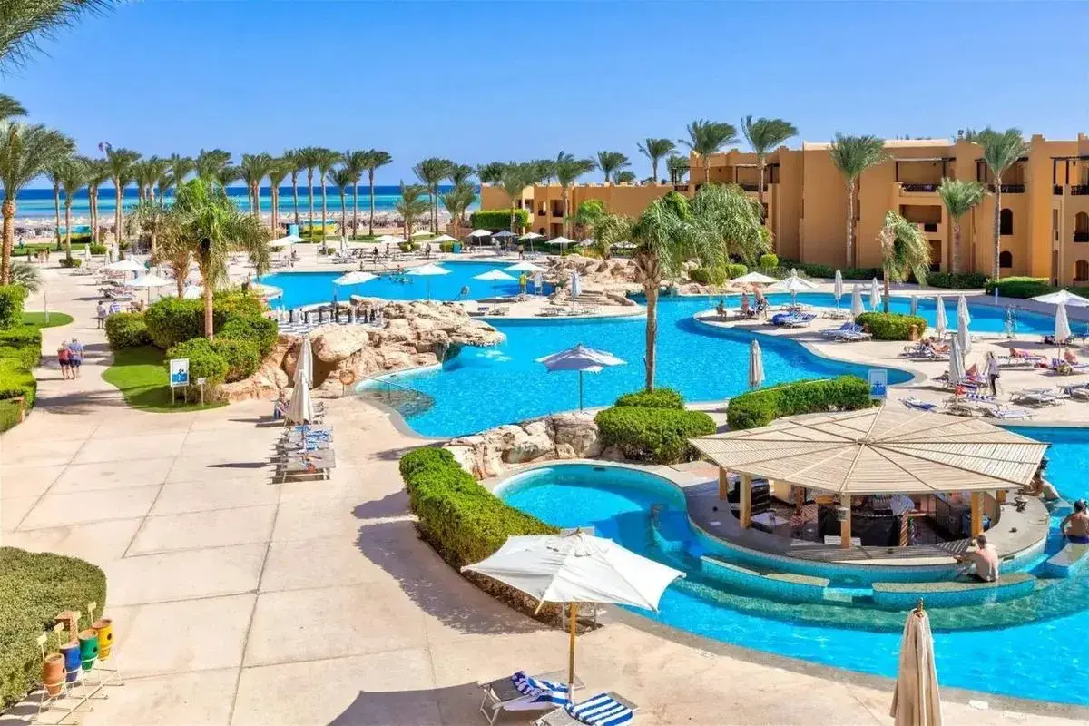 Słoneczny dzień w Stella Beach Resort & Spa Makadi Bay. Goście relaksują się przy basenach, pod palmami i parasolami.