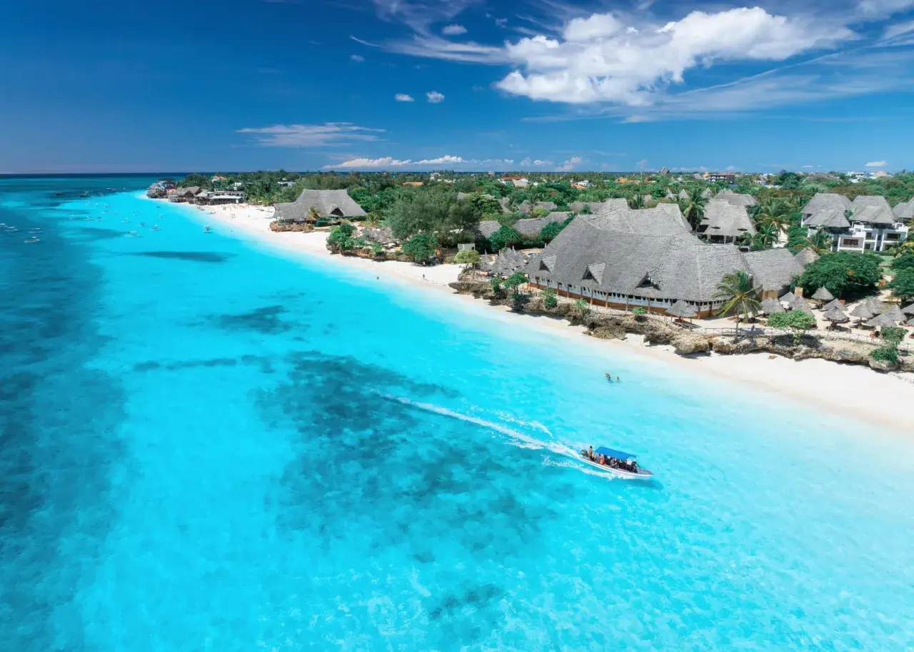 Idealny dzień na Zanzibarze: turkusowa woda, biała plaża i łódź pełna ludzi.