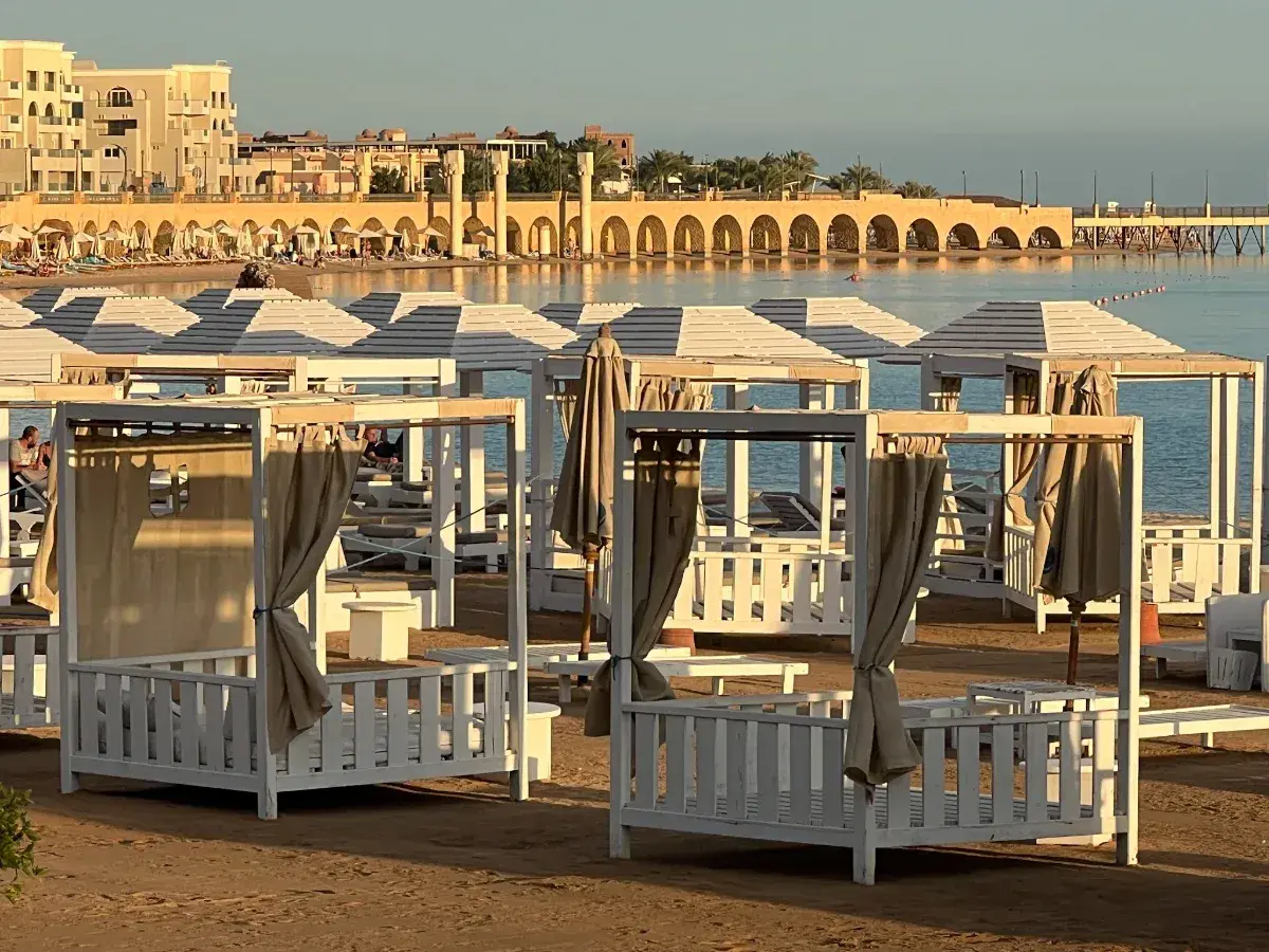 Piękna pogoda w Egipcie w styczniu. Leżaki i baldachimy na plaży, w tle budynki i morze.