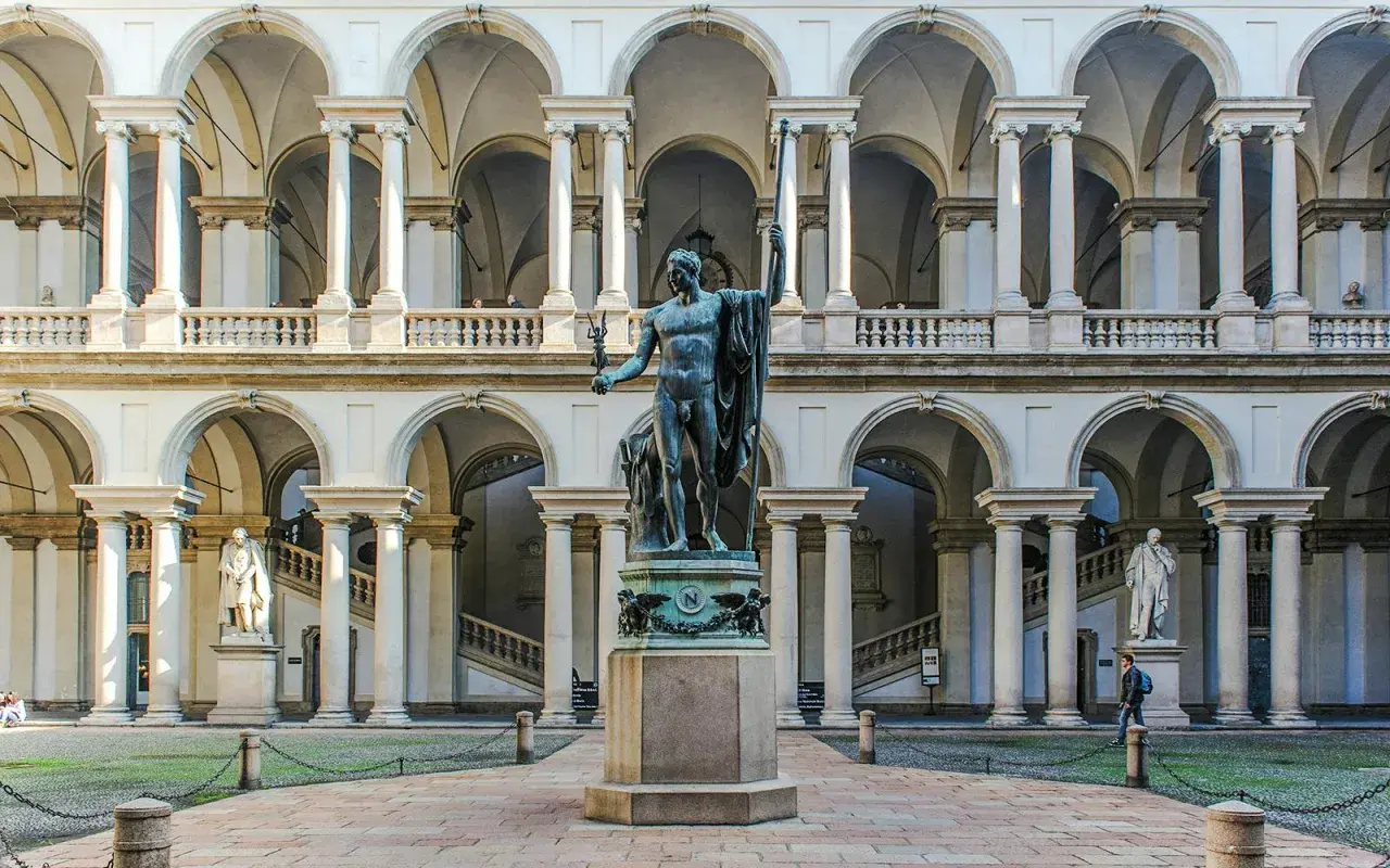 Dziedziniec Pinacoteca di Brera z rzeźbą w centrum i arkadowymi galeriami.