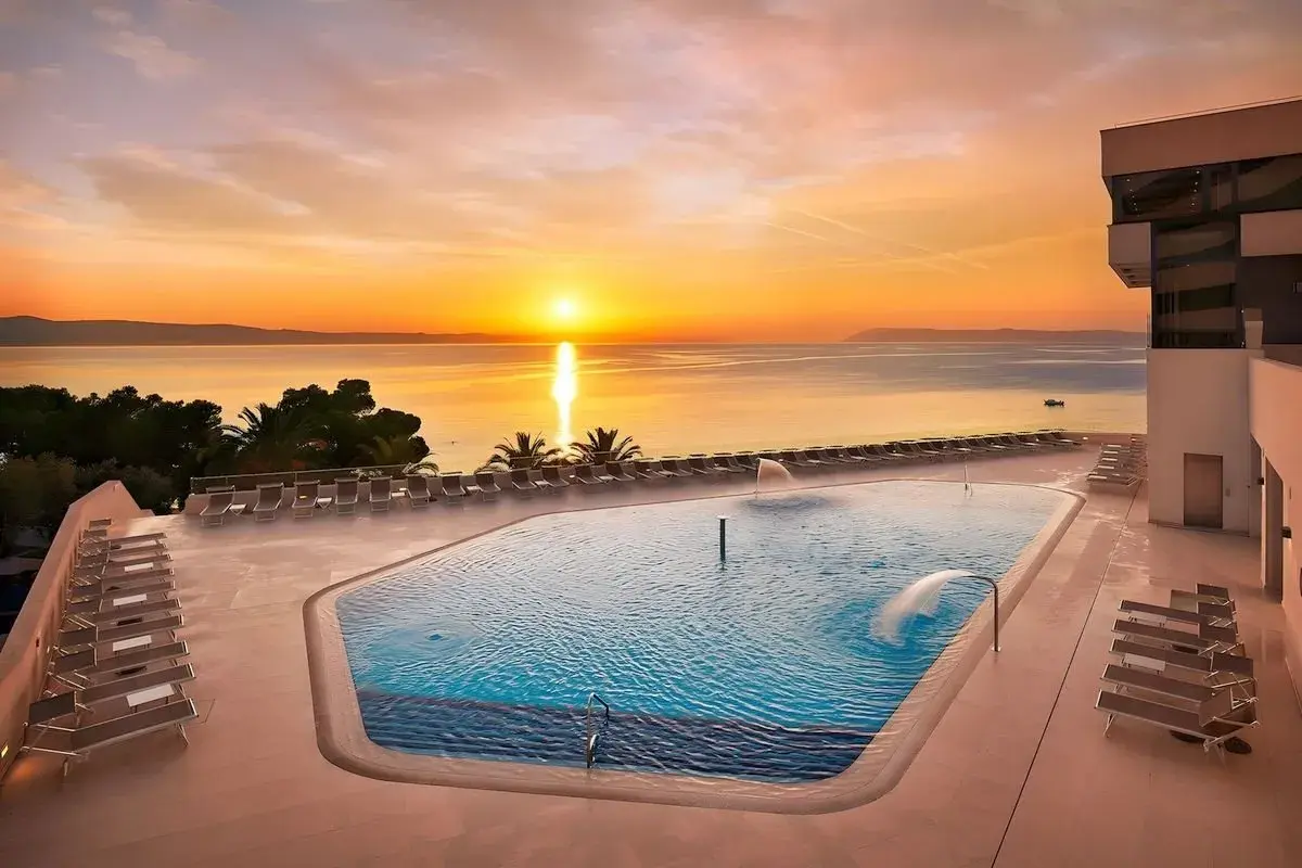 Zachód słońca nad basenem w Medora Auri Family Beach Resort. Woda w basenie lśni, a leżaki czekają na gości.