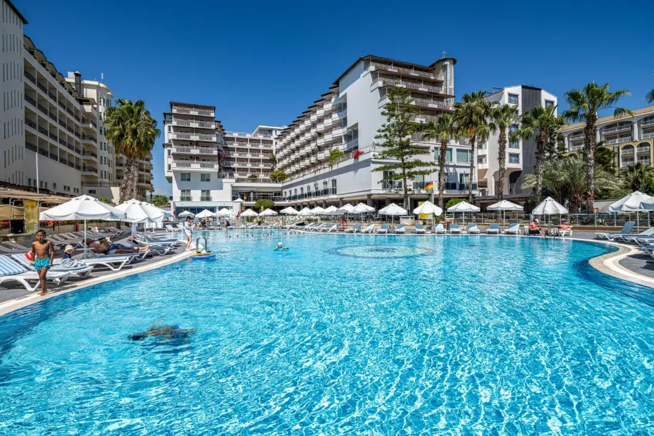 Basen hotelowy Granada Luxury Okurcalar, z leżakami, parasolami i palmami. Dzieci pluskają się w wodzie.