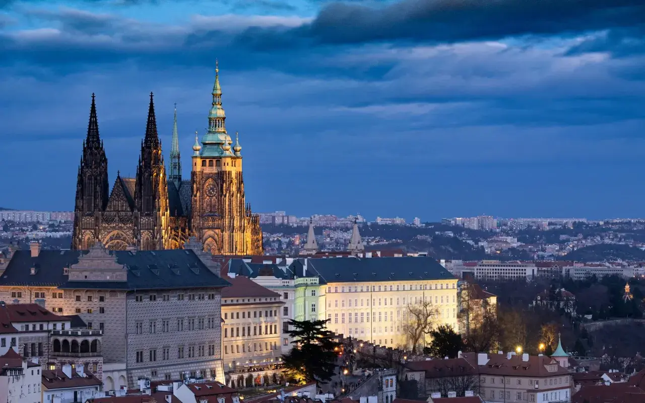 Imponujący zamek w Pradze o zmierzchu, z majestatyczną katedrą i oświetlonymi budynkami na pierwszym planie.